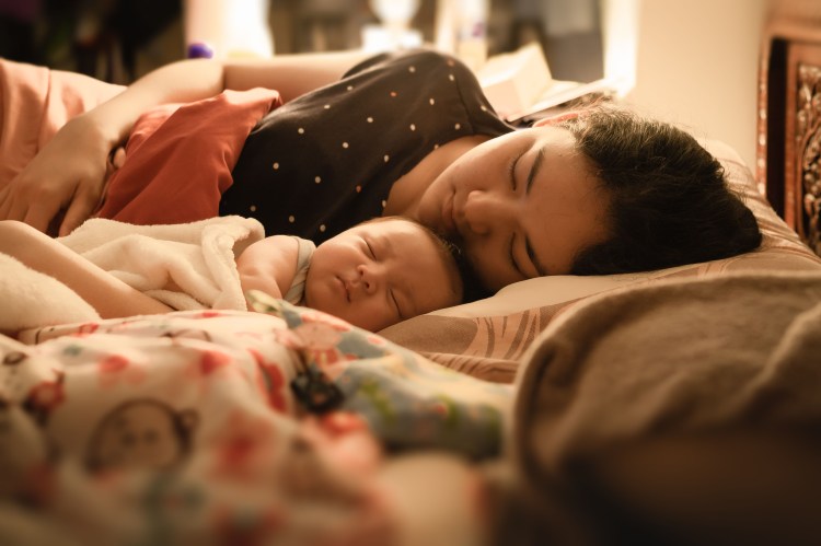 Asian mother sleeping peacefully  in bed next to her newborn baby